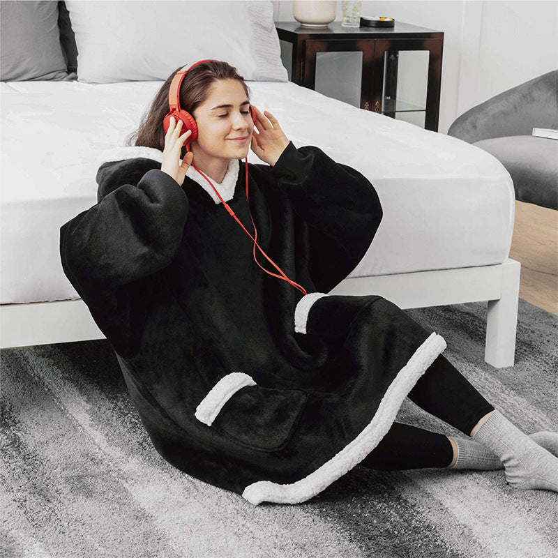 Woman in the black Wearable Blanket sitting by a bed with headphones on